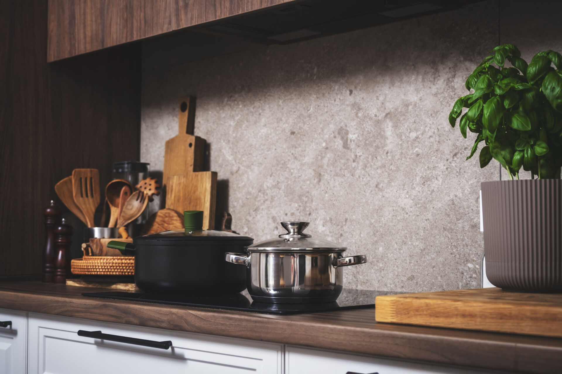 Cozy modern kitchen with cooking utensils, pots, cutting boards on wooden countertop with porcelain stoneware kitchen backsplash